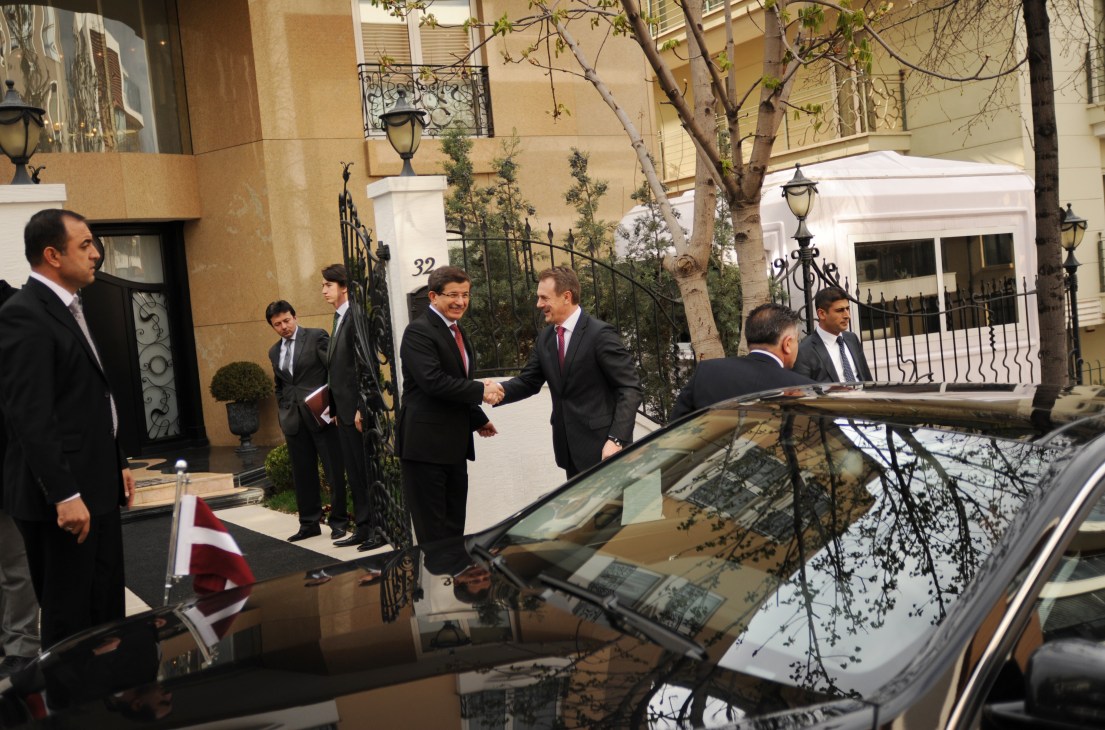 Ahmet Davutoglu shakes hands with the Latvian foreign minister outside a building with security and aides present.