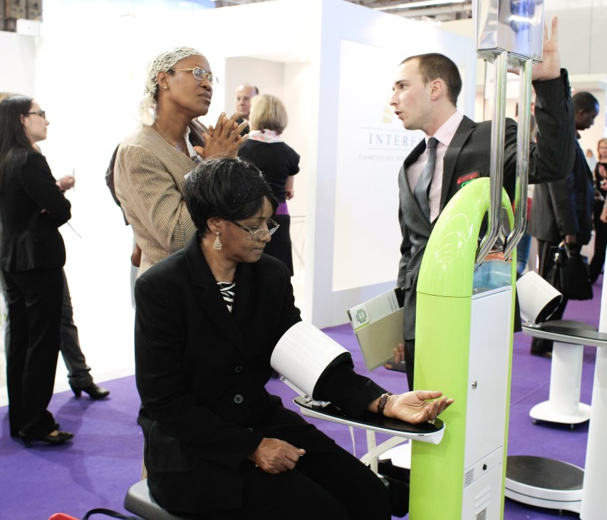 Woman testing a lime-green blood-pressure monitor at a trade fair booth.