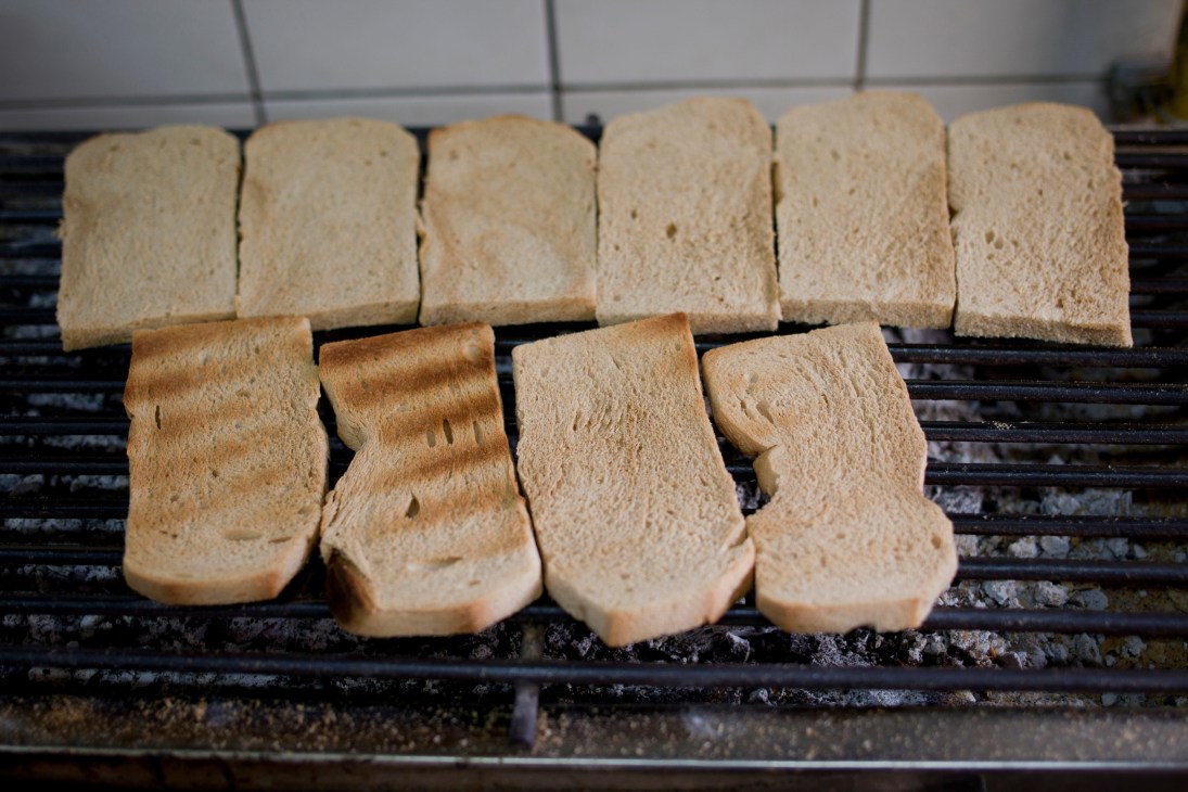 Slices of bread toasting on a grill, some untoasted and others with golden-brown char marks.