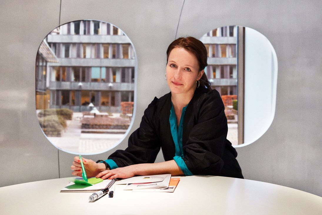 Anette Væring, designer at Mindlab, seated at a desk in The Mind workspace with circular windows behind her.