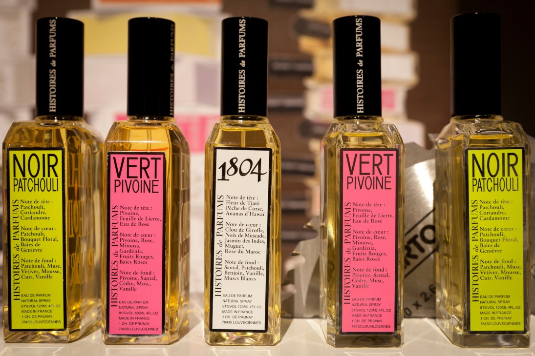 Row of Histoires de Parfums fragrance bottles with black caps and colorful labels displayed at trade fair.