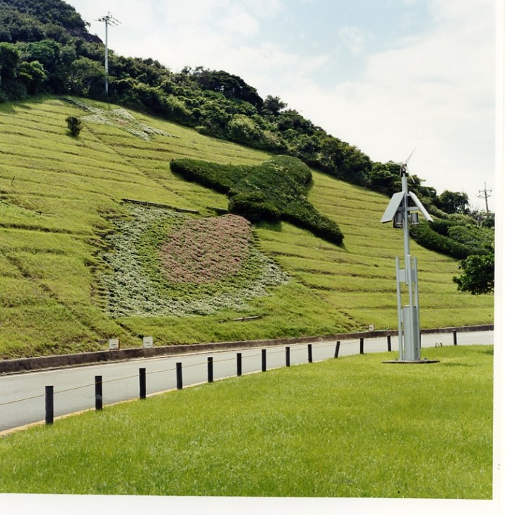 A rocket-shaped topiary sculpture cut into green grass beside a paved path on Tanegashima island.