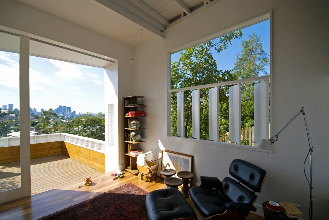 Modern living room with exposed ceiling, black lounge chairs, wooden deck, and views of Brisbane cityscape through large windows.