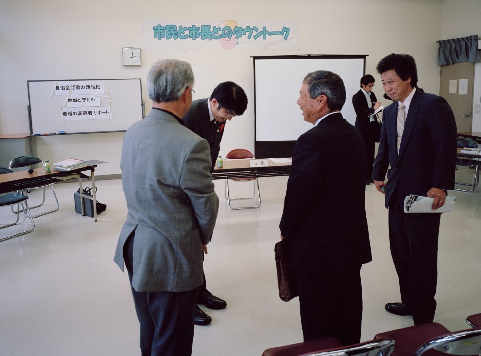Tomihisa Taue, mayor of Nagasaki, talks with citizens in a meeting room with Japanese text on the wall.