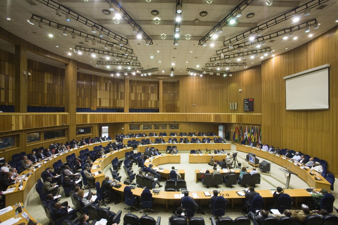 Wide view of the African Union chamber in Addis Ababa with curved tiered seating, wood paneling, and numerous delegates seated during a session.