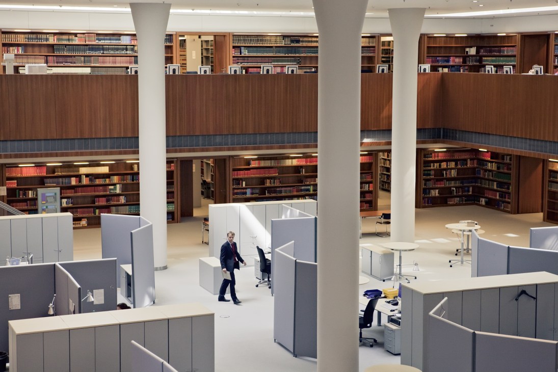 Interior library space with wooden bookshelves, white columns, and modern office cubicles in the German Federal Foreign Office.