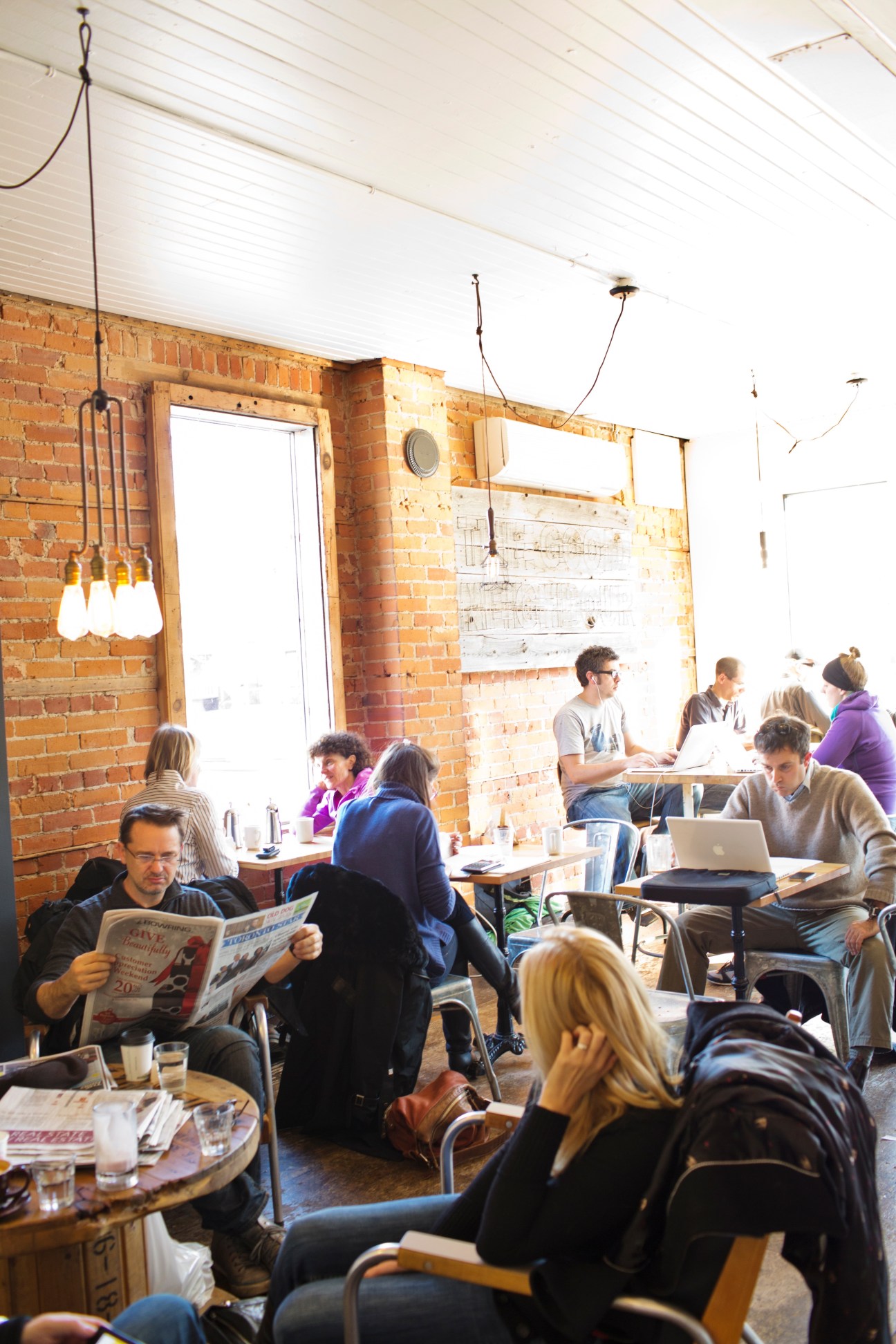 Customers sit at tables inside The Good Neighbour café with exposed brick walls and pendant lighting.