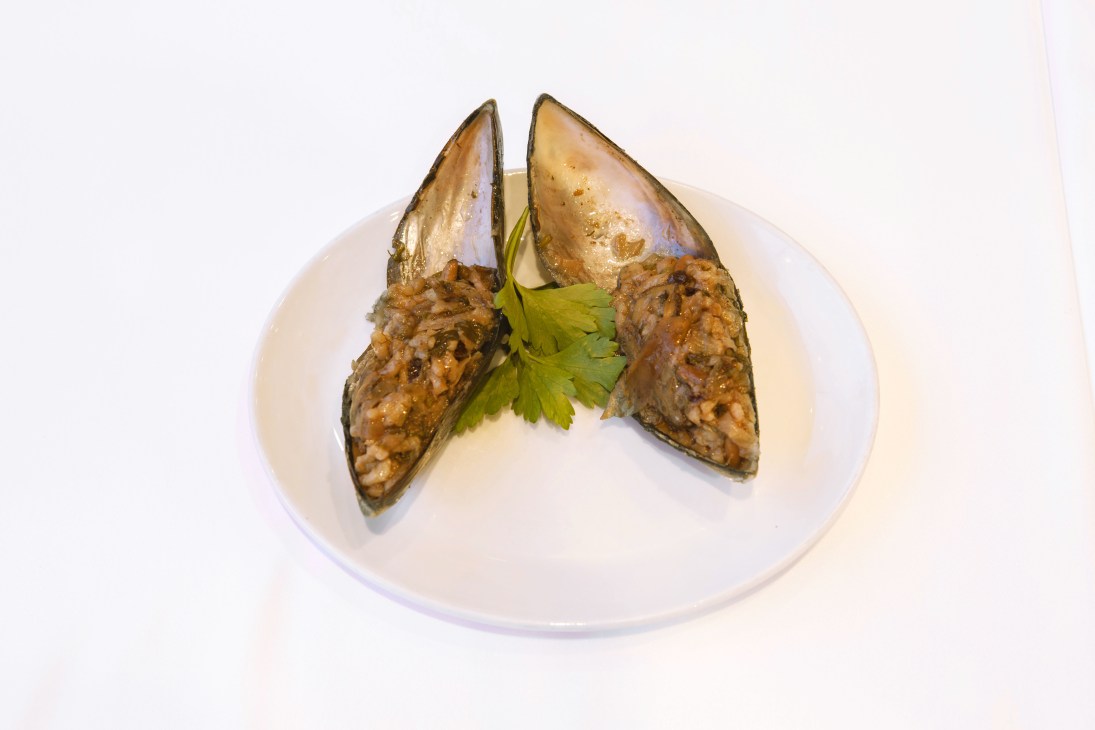 Two mussels filled with rice and garnished with parsley on a white plate.