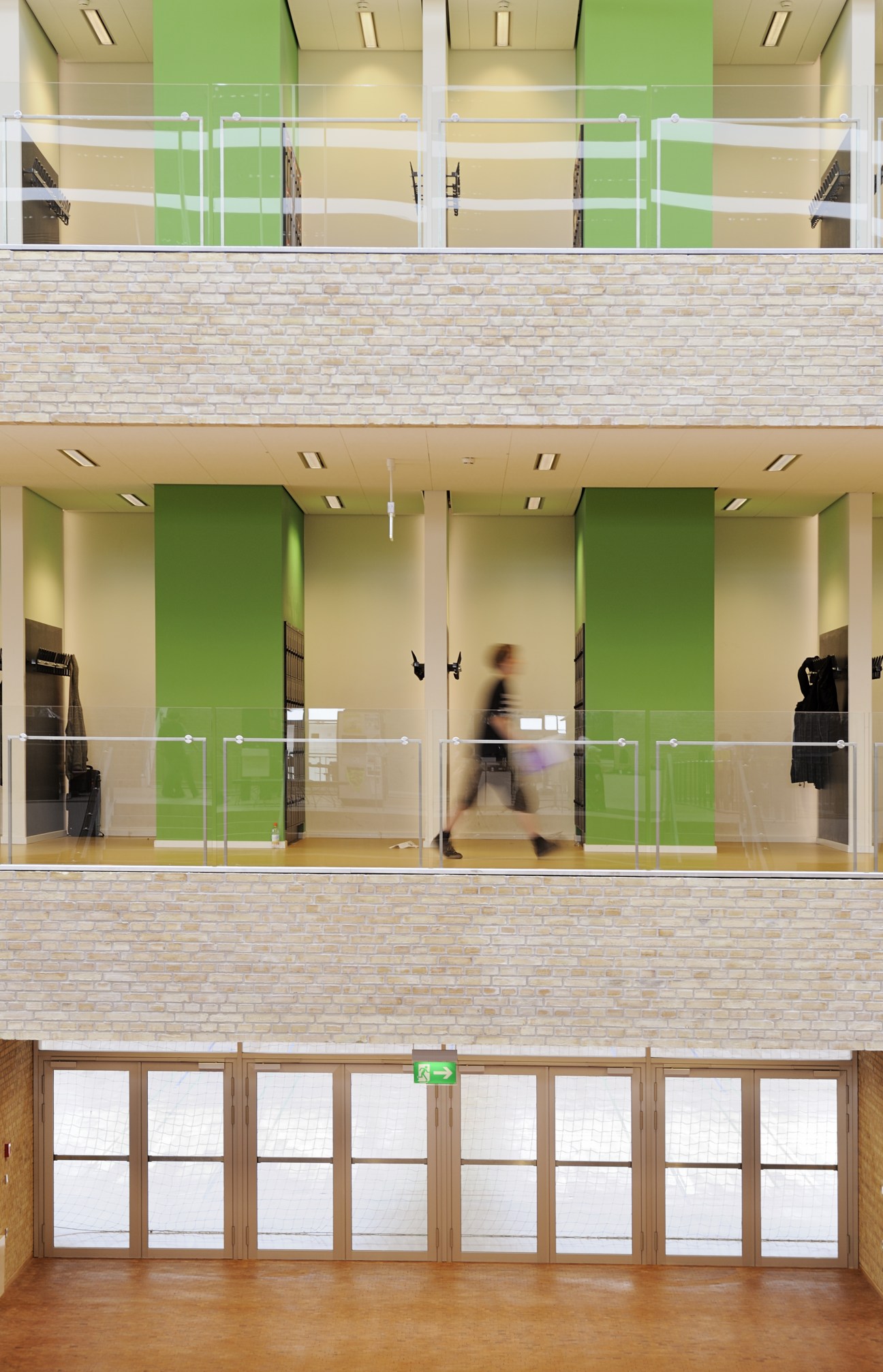 Multi-story school interior with green and cream walls, glass balconies, and brick facade with natural materials.