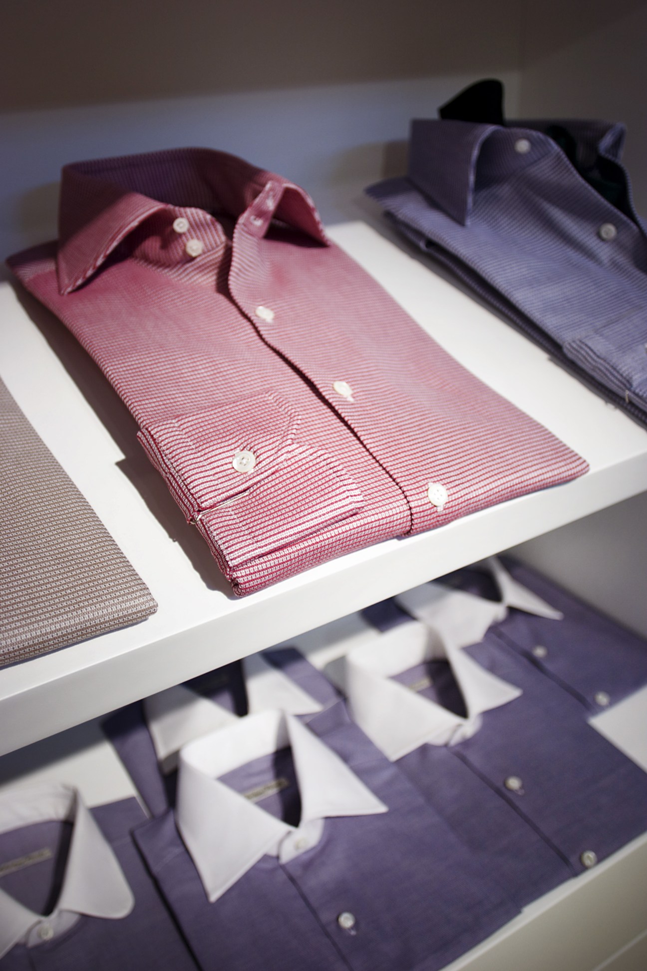 Aertex shirts by Salvatore Piccolo in pink and purple displayed on white shelves.