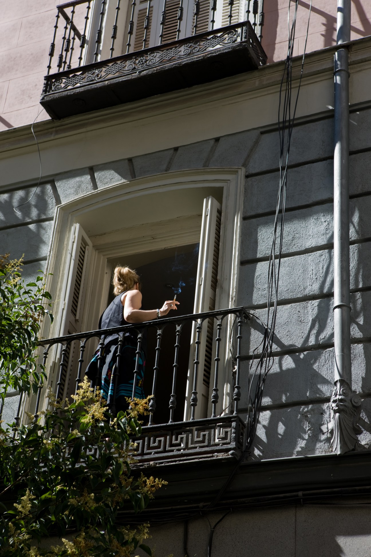 Woman standing on ornate iron balcony of a Bourbon-era Madrid apartment building.