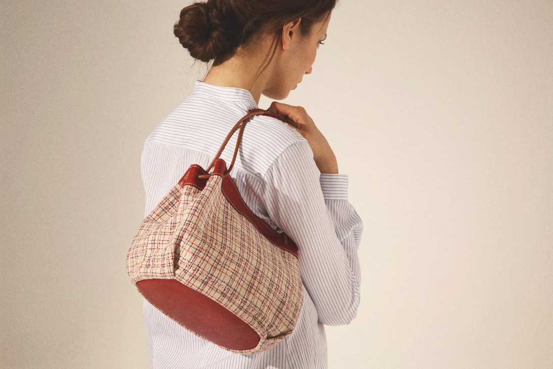 Woman wearing a white striped shirt carrying a red and cream checked Iroe textile bag.