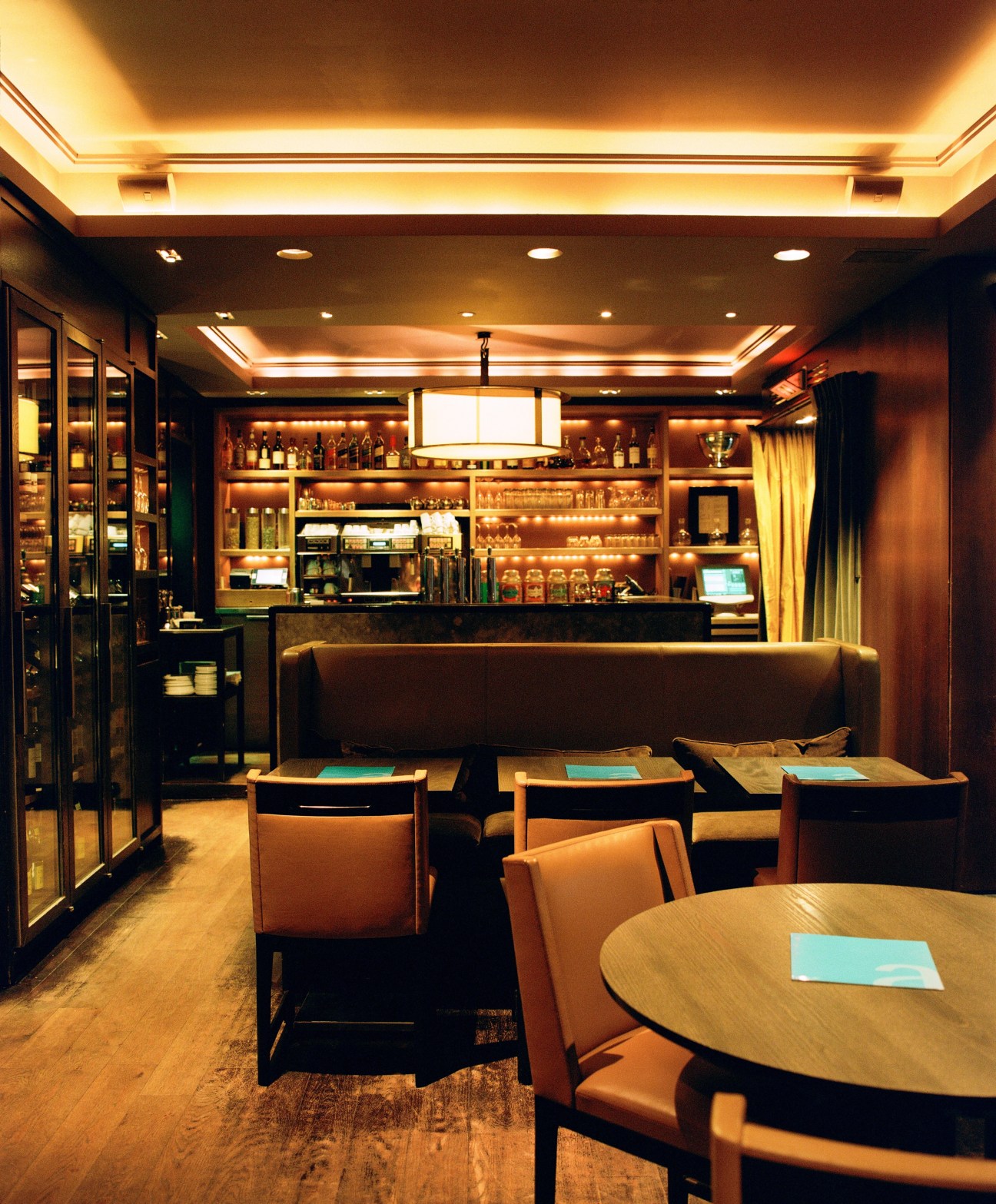 Interior of Café de l'Alma with warm lighting, wooden tables, leather banquette seating, and illuminated bar shelving.