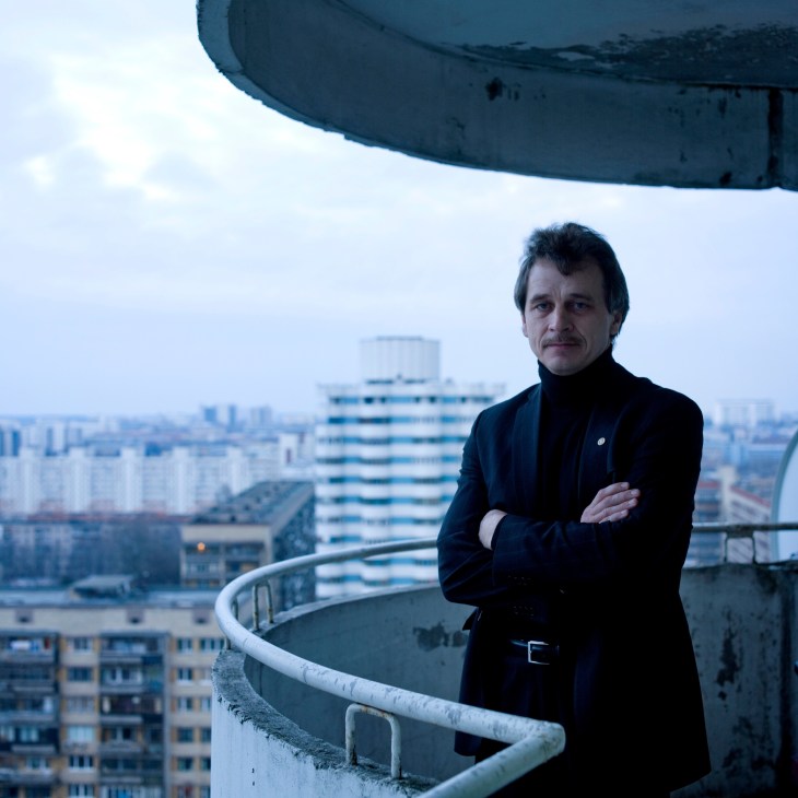 Opposition leader Alexander Lebedko standing on a high balcony overlooking Minsk cityscape.