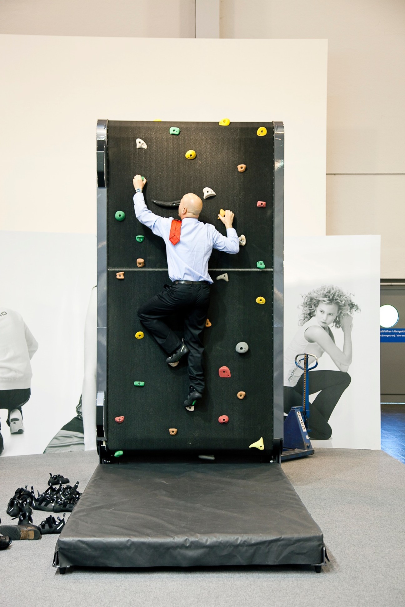 Man in business attire climbing an indoor wall simulator with colorful handholds.