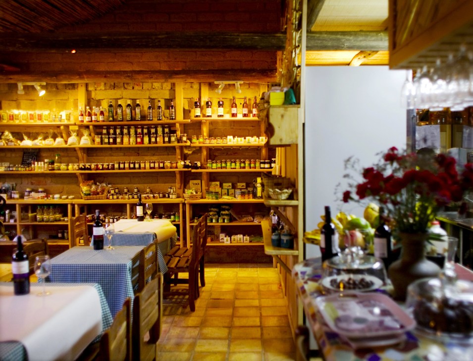 Interior of Savia restaurant with wooden shelves stocked with bottles, tables with blue checkered tablecloths, and flowers on display.