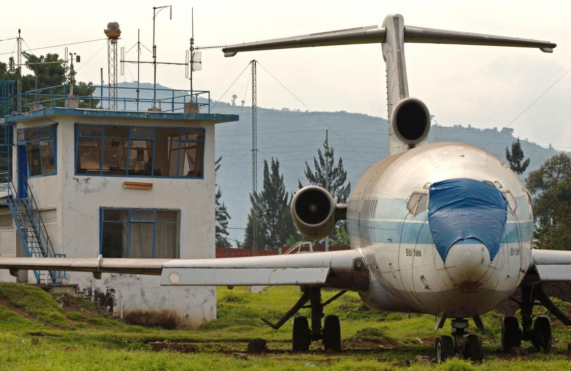 Abandoned plane with blue accents next to control tower at Goma airport, mountains visible in background.