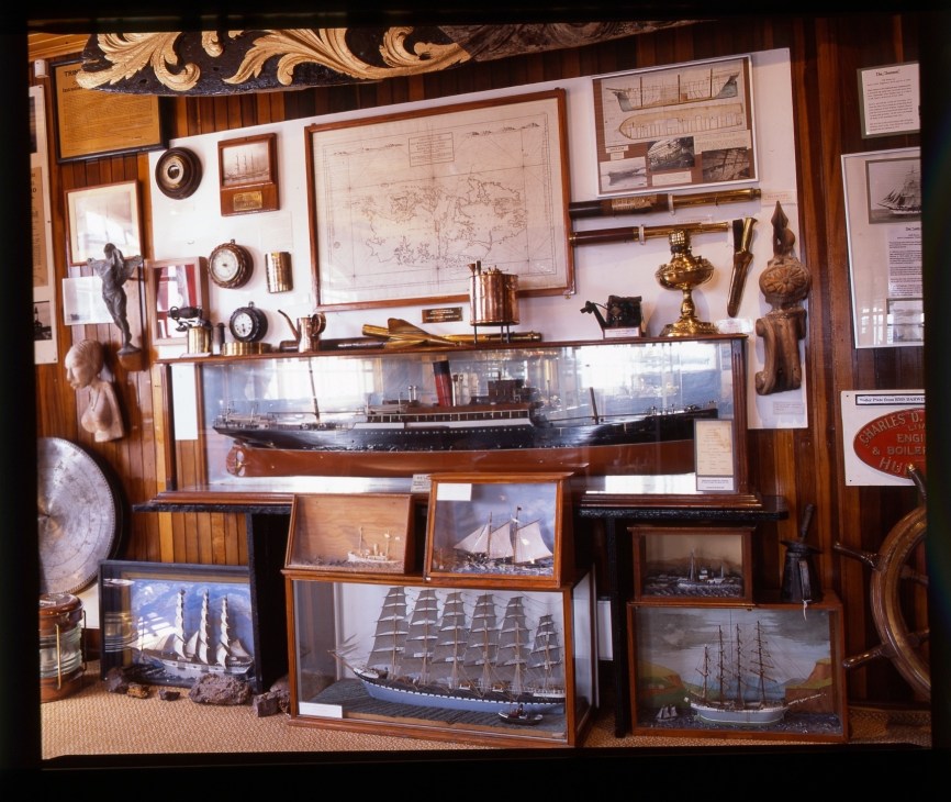 Museum display of maritime history with wooden-framed ship models, nautical instruments, maps, and brass artifacts.