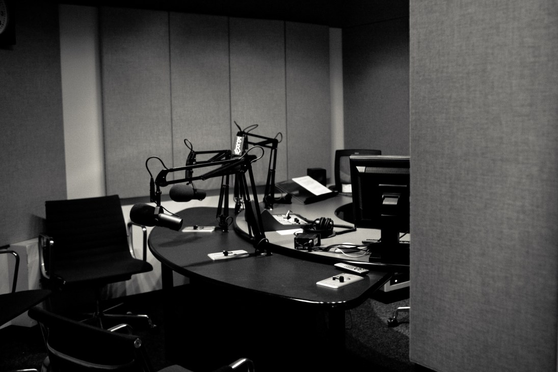 Black and white photograph of KCRW's interview studio showing microphone setup and broadcasting equipment on desk.
