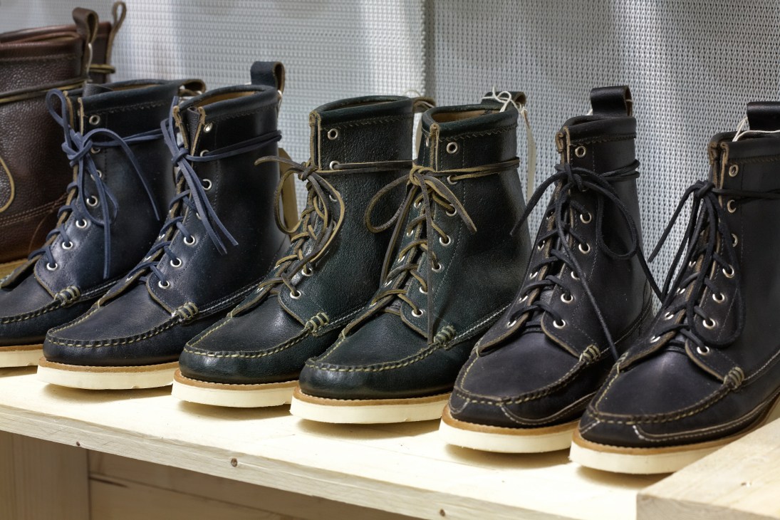 Row of black leather lace-up boots with cream-colored soles displayed on a white shelf.
