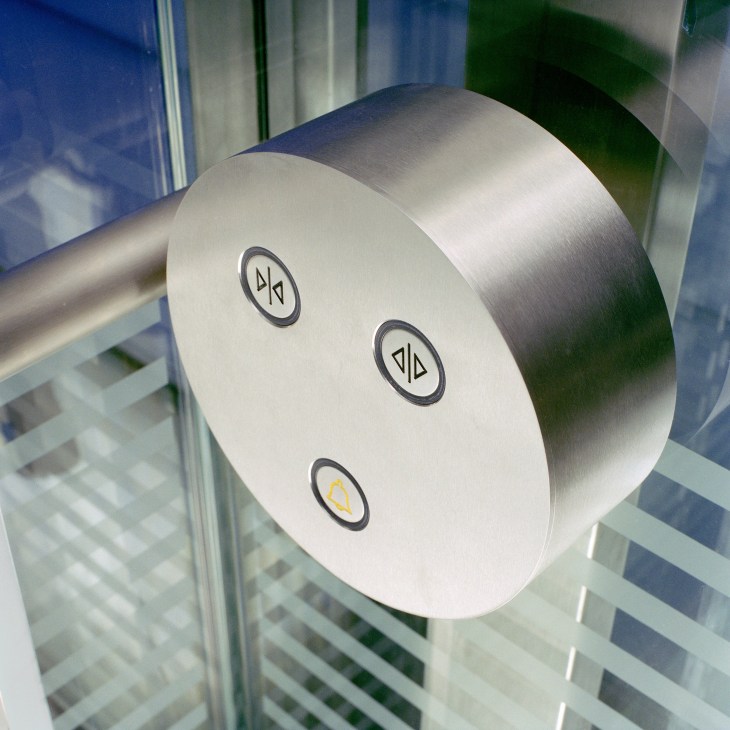 Close-up of a circular stainless steel elevator control panel with three illuminated buttons featuring directional and floor symbols.