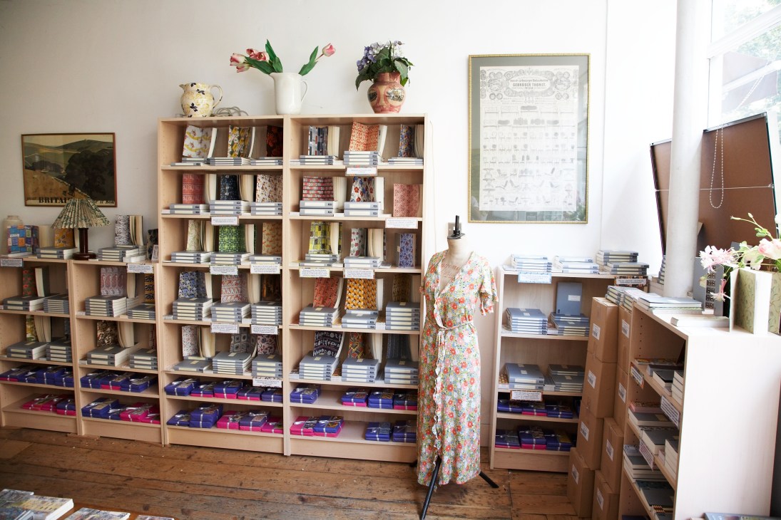 Interior of Persephone bookshop showing wooden shelves displaying books with colorful spines and a mannequin wearing a floral dress.