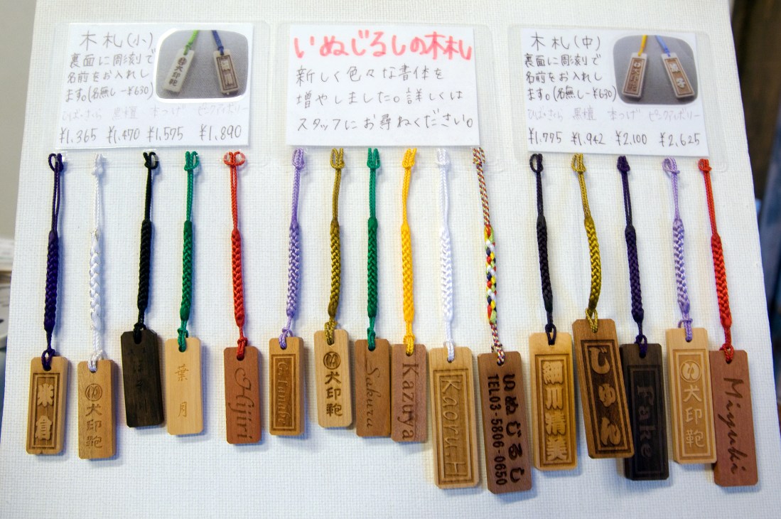 Wooden name tags with colored cords and Japanese text, displayed on white surface with price information cards.
