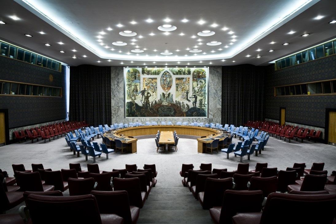UN Security Council meeting hall with circular seating arrangement and ornate mural backdrop.