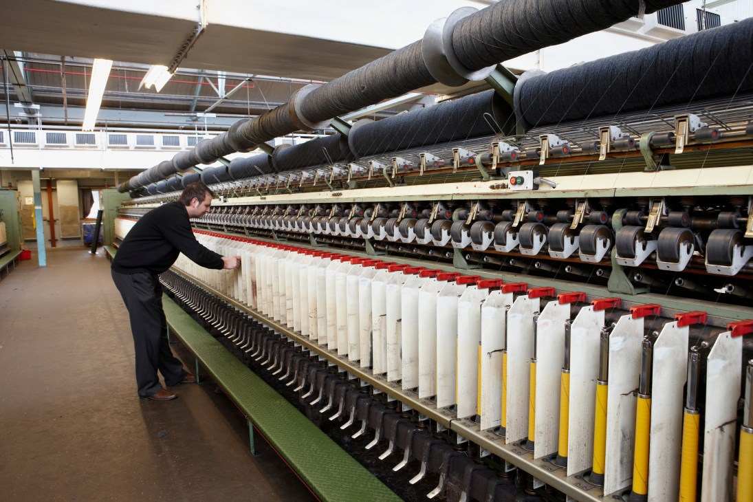 Worker inspects cashmere thread on industrial spinning machinery at Johnstons factory in Scotland.