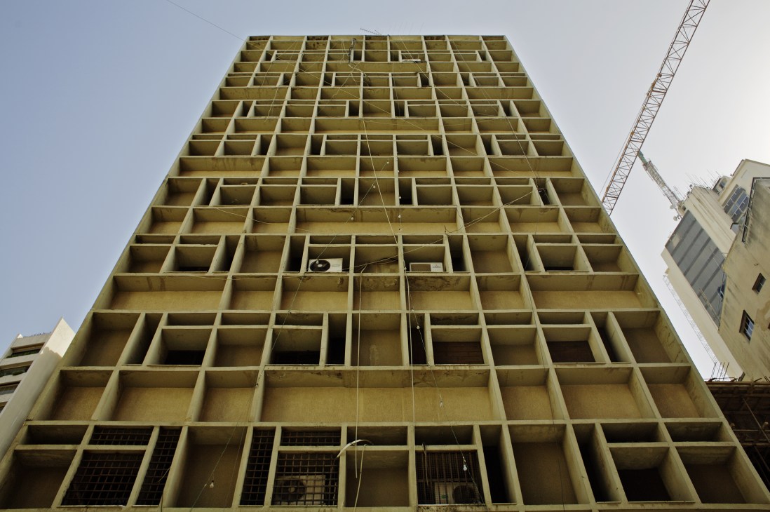 Brutalist concrete high-rise under construction with repetitive grid of empty window openings and metal scaffolding.