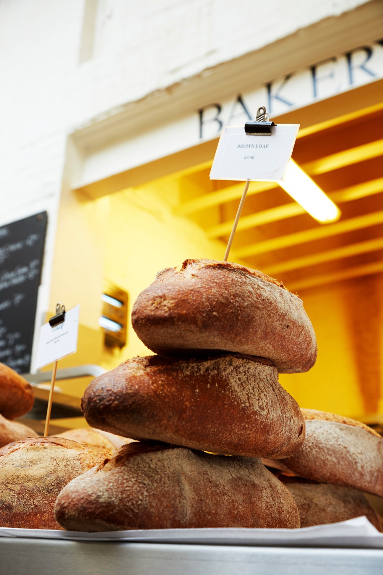 Stacked brown loaves with price label at St John bakery counter with yellow shelving behind.