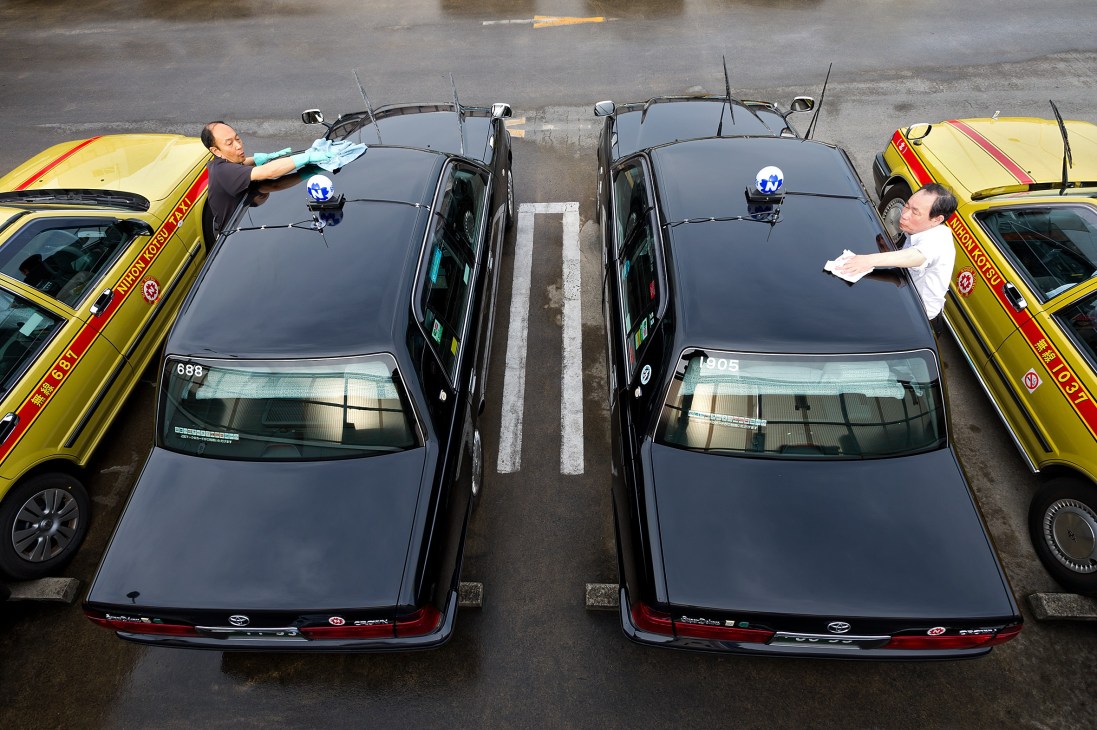Drivers cleaning black and yellow Tokyo taxis in a parking depot.