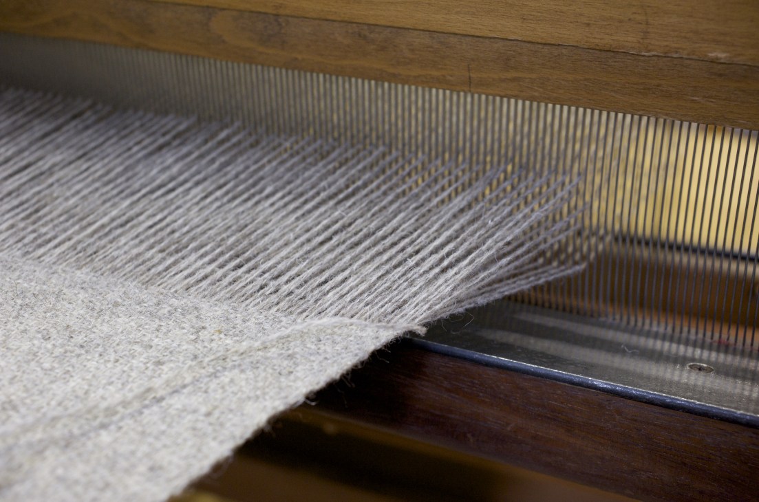 Close-up of woven lambswool cloth on a traditional wooden loom showing interlaced threads.