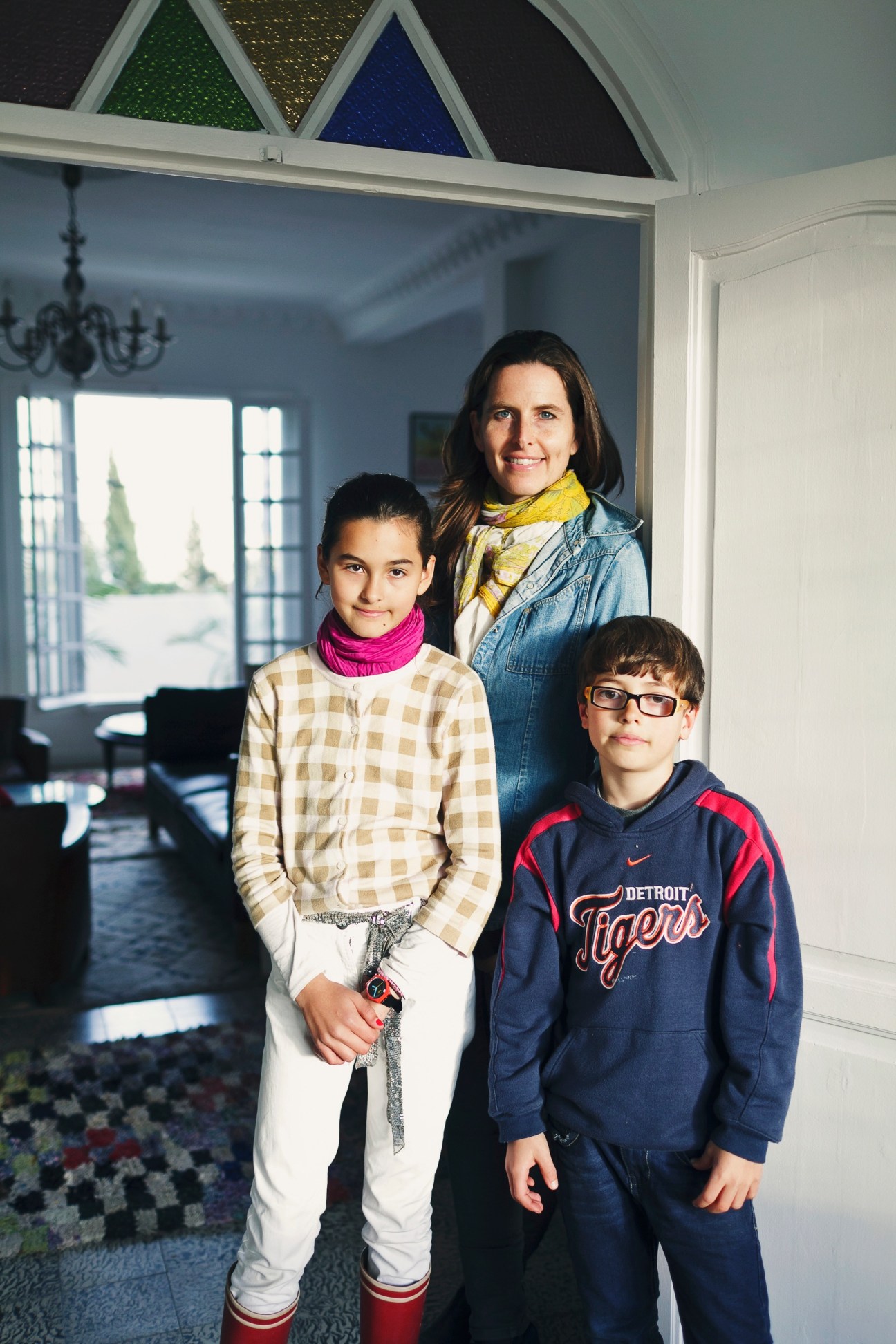 Julie Klear poses with her two children in a bright modern living room with triangular windows above.