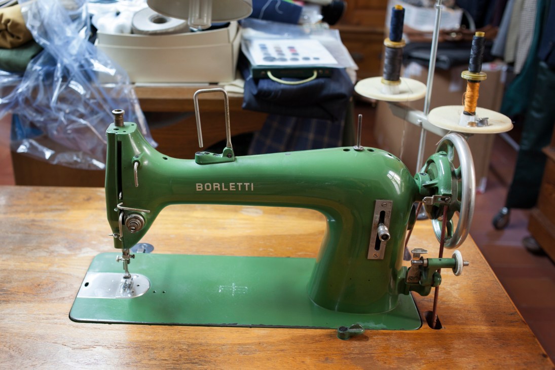 A green Borletti sewing machine with wooden base on a work table at Liverano & Liverano tailoring studio.