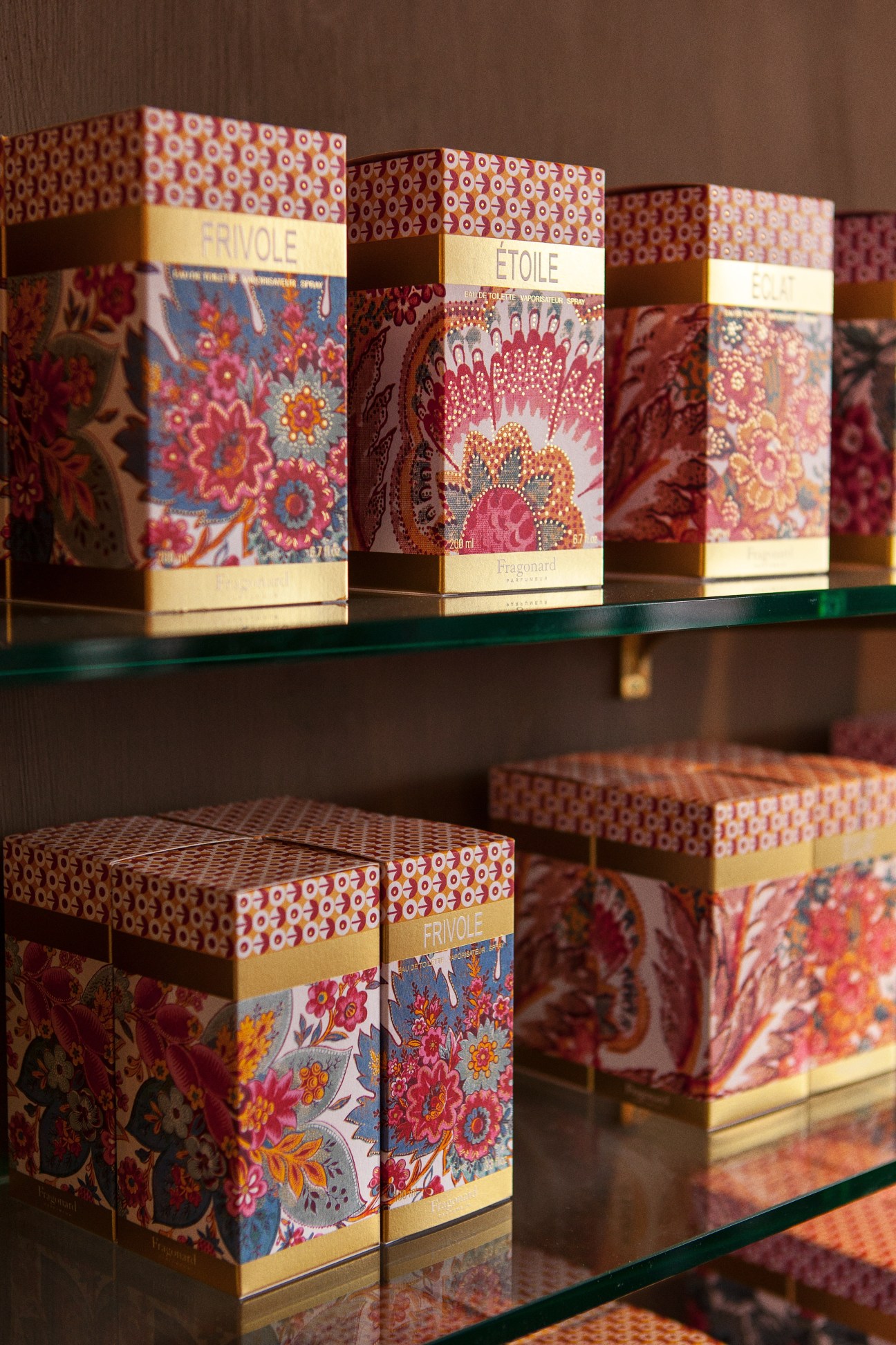 Fragonard perfume boxes with decorative floral patterns displayed on glass shelves.