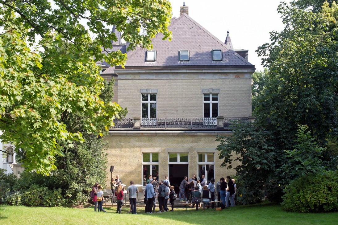 Attendees gather outside a 19th-century brick mansion with manicured gardens at the Indiecon conference in Hamburg.