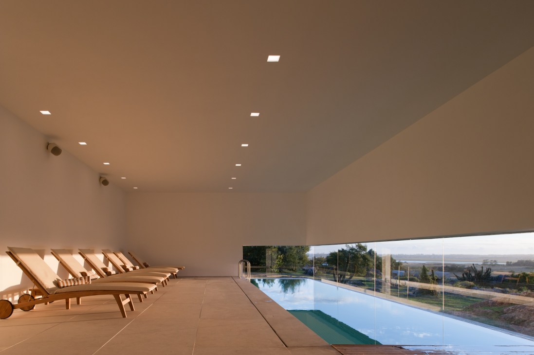 Modern spa interior with wooden loungers, pool, and expansive landscape views through floor-to-ceiling windows.