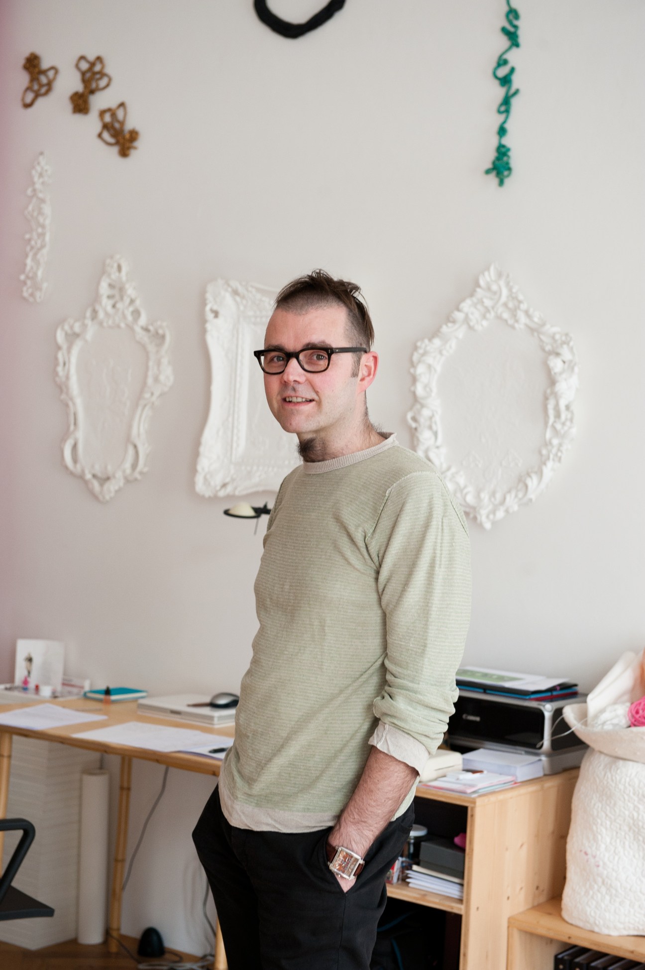 Artist and designer Heiri Häfliger poses in his studio workspace with decorative wall art.