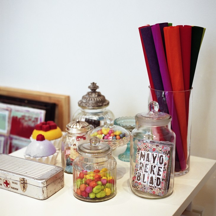 Colorful display in Anna Lena Mayor Ekeblad's shop featuring glass jars with candies, rolled fabrics, and decorative items.