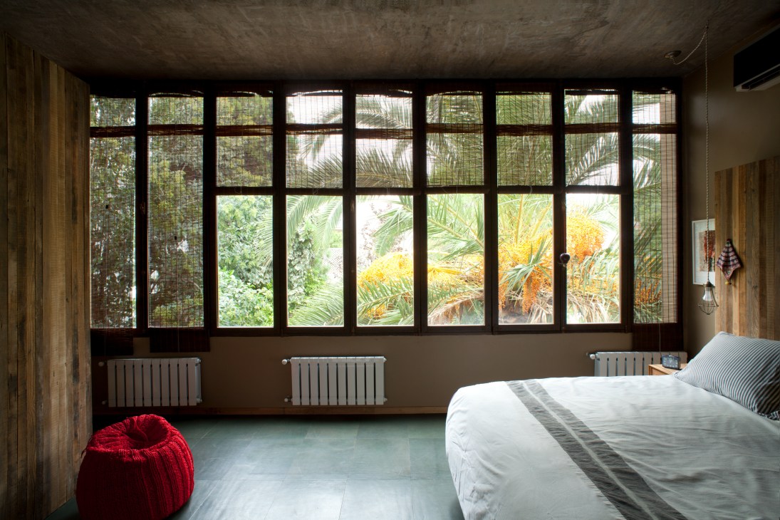 Bedroom with large gridded windows overlooking a palm tree and garden terrace.