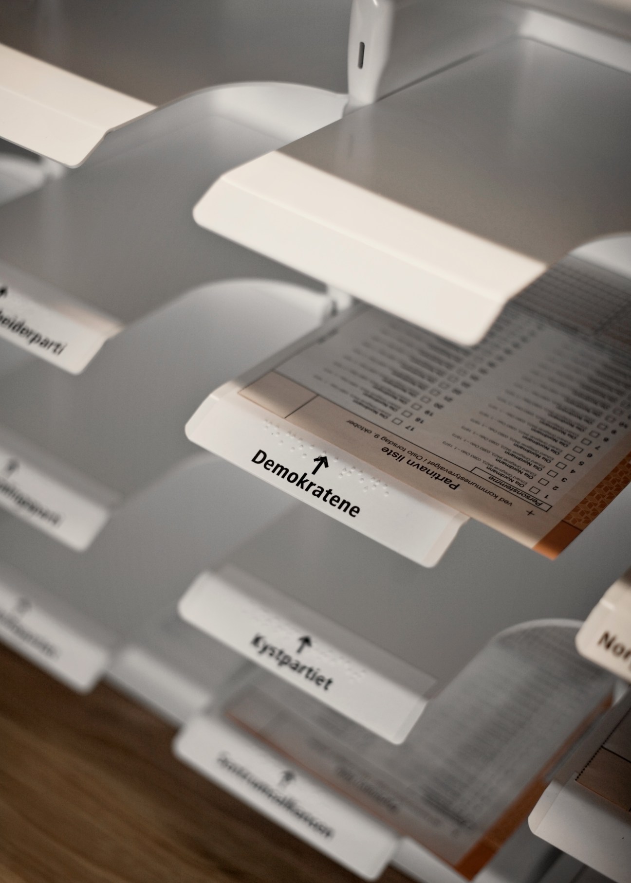 Close-up of removable ballot paper trays with Braille labels and directional arrows in Norwegian voting booth design.