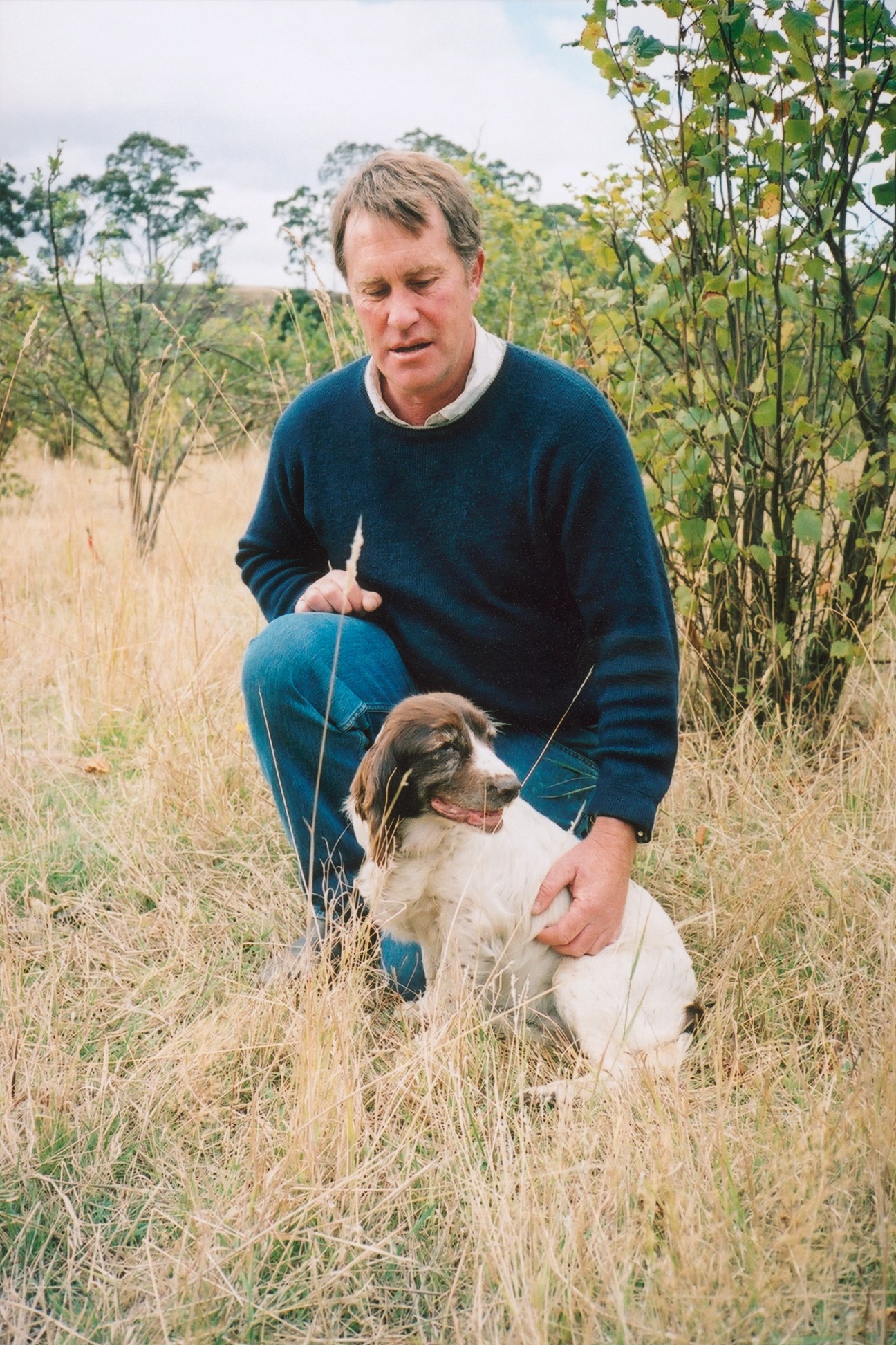 Duncan Garvey crouches in a field with his truffle-hunting dog Pip beside him.