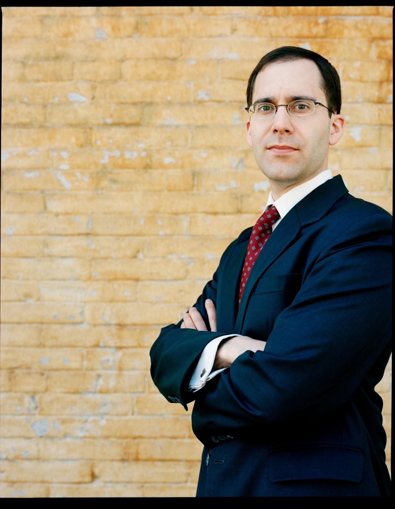 James Liotta, an American expat lawyer with Lehman, Lee & Xu, poses against a brick wall wearing glasses and a dark suit with red tie.