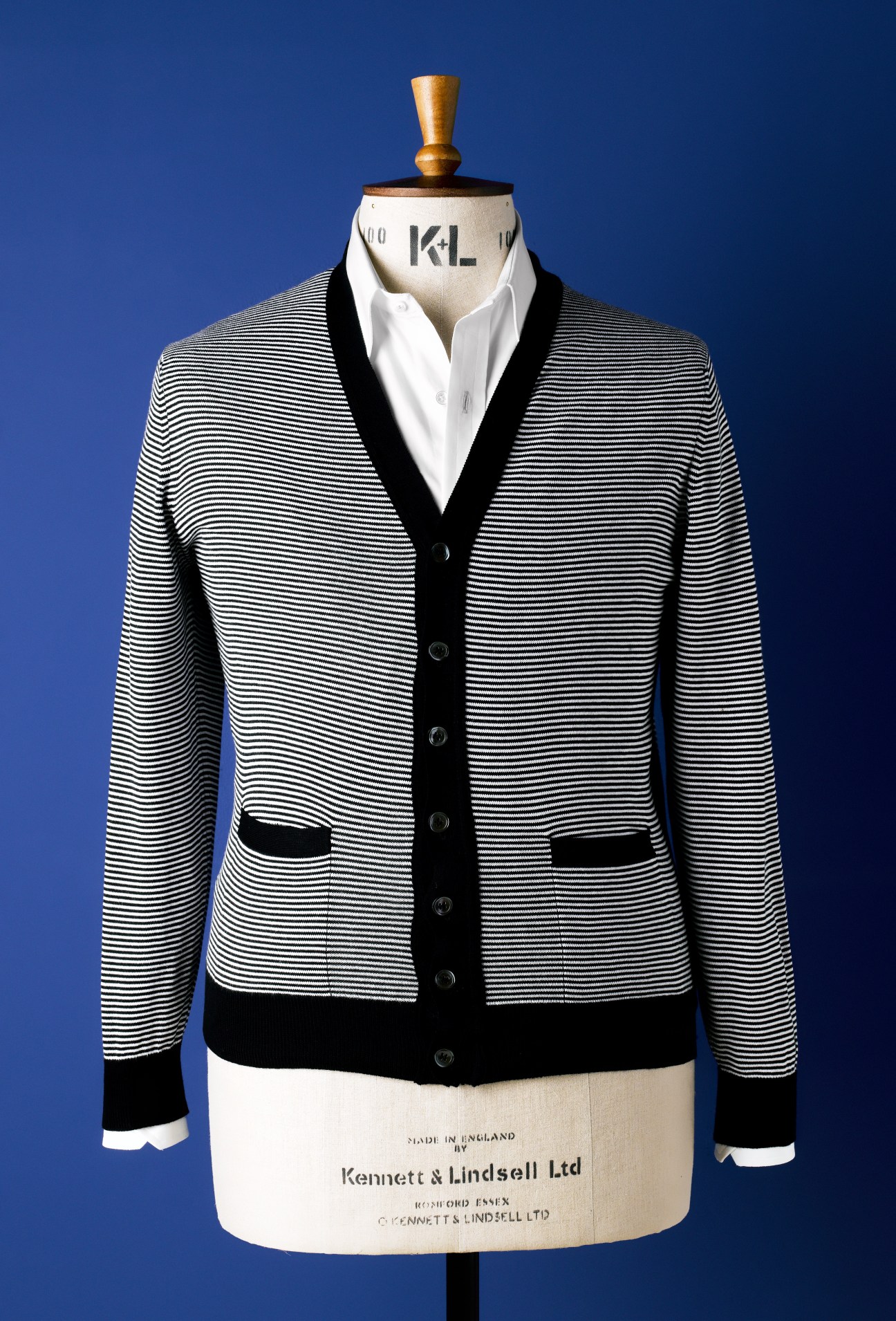 Striped cardigan with black trim on a dress form against a blue background.