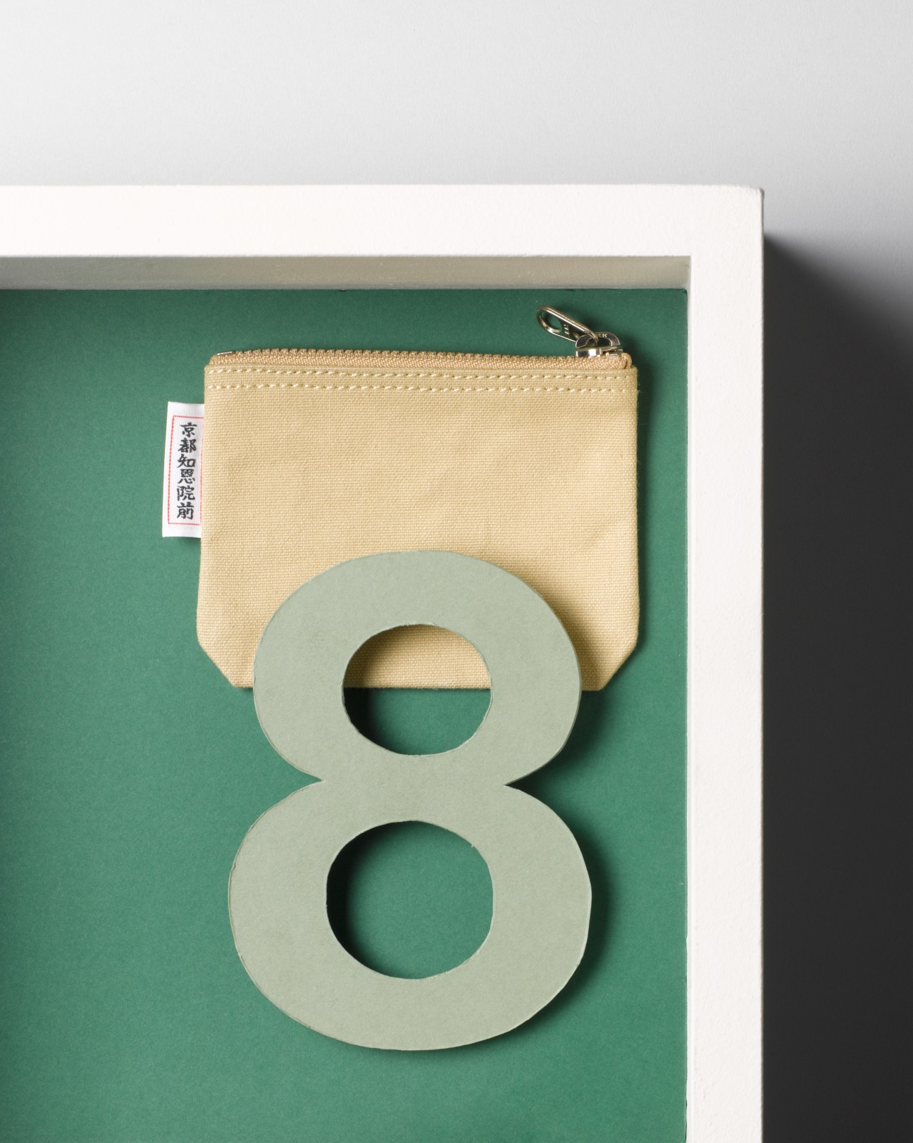 Ichizawa Hanpu cream canvas coin purse with metal clasp on green background.