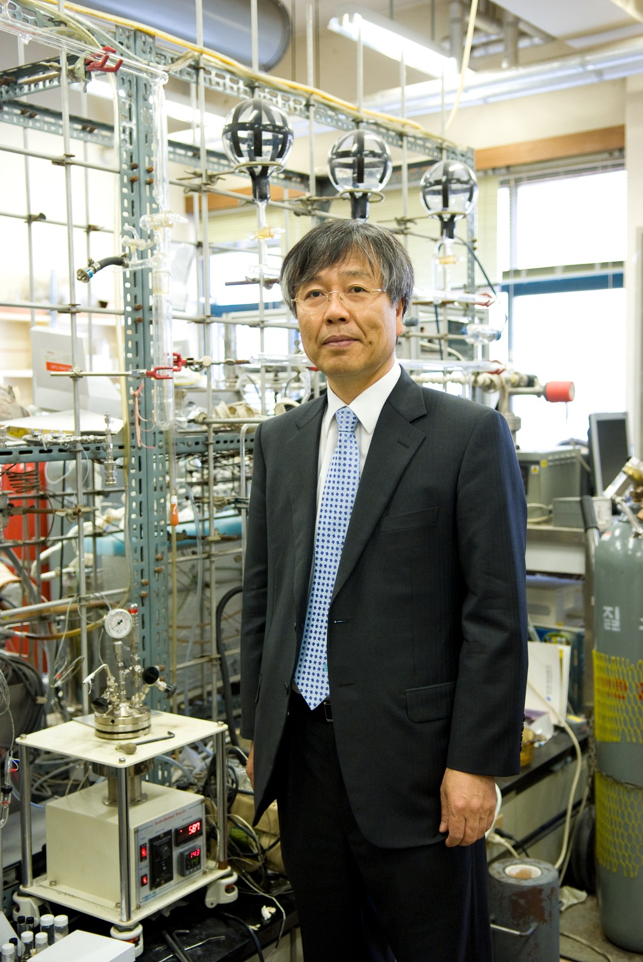 Ryong Ryoo, professor of chemistry, stands in a laboratory with experimental equipment behind him.