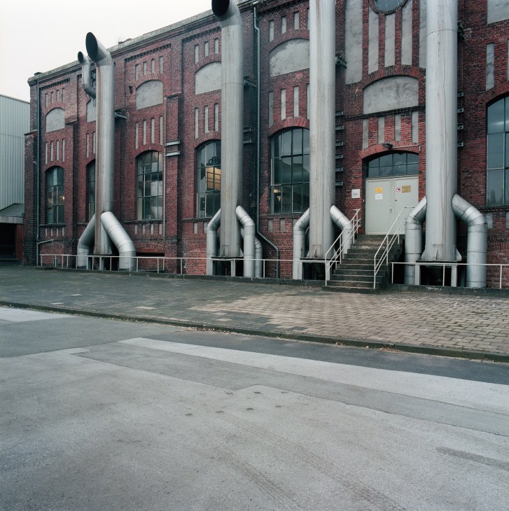Red brick industrial building with large grey metal pipes running up its facade.