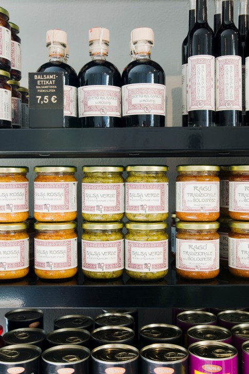 Shelves stocked with Italian balsamic vinegar bottles and colorful jars of sauces and preserves with decorative labels.