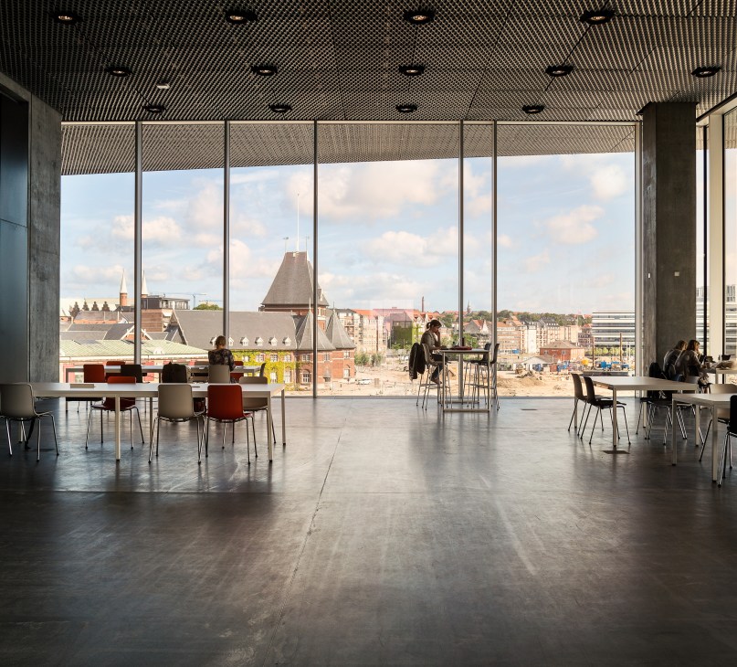 Modern library interior with floor-to-ceiling windows overlooking Aarhus cityscape and construction sites.